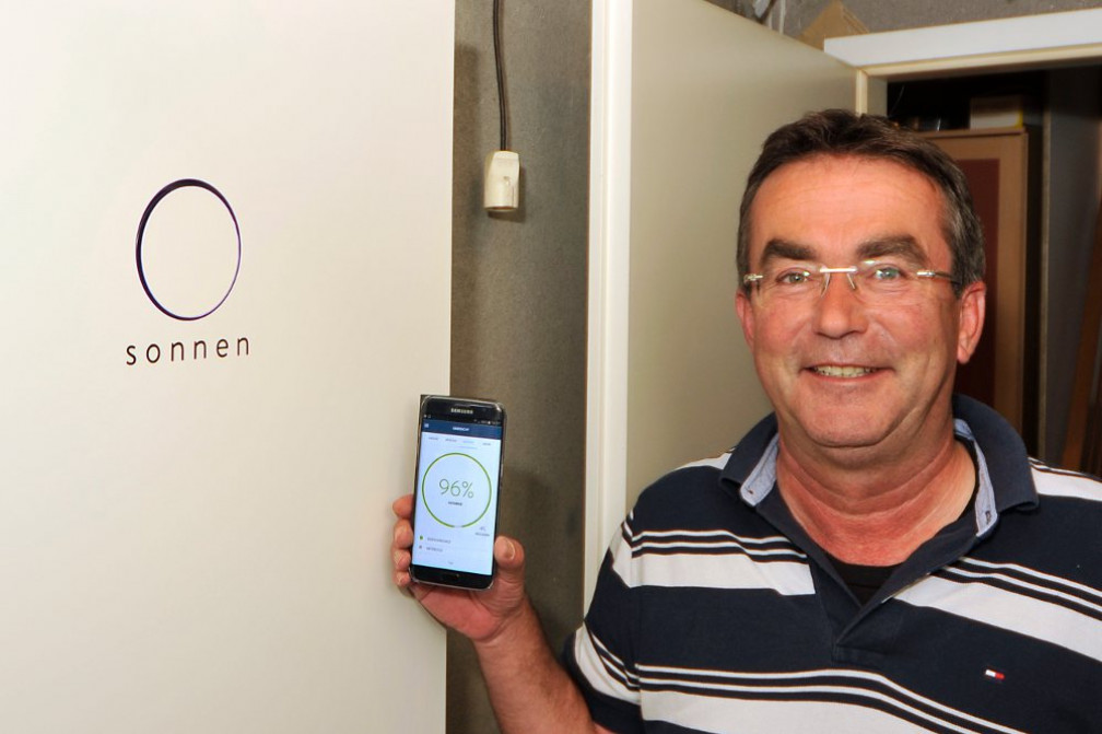 sonneBatterie Kunde vor seinem Stromspeicher mit Handy auf dem sie monitoring App geöffnet ist